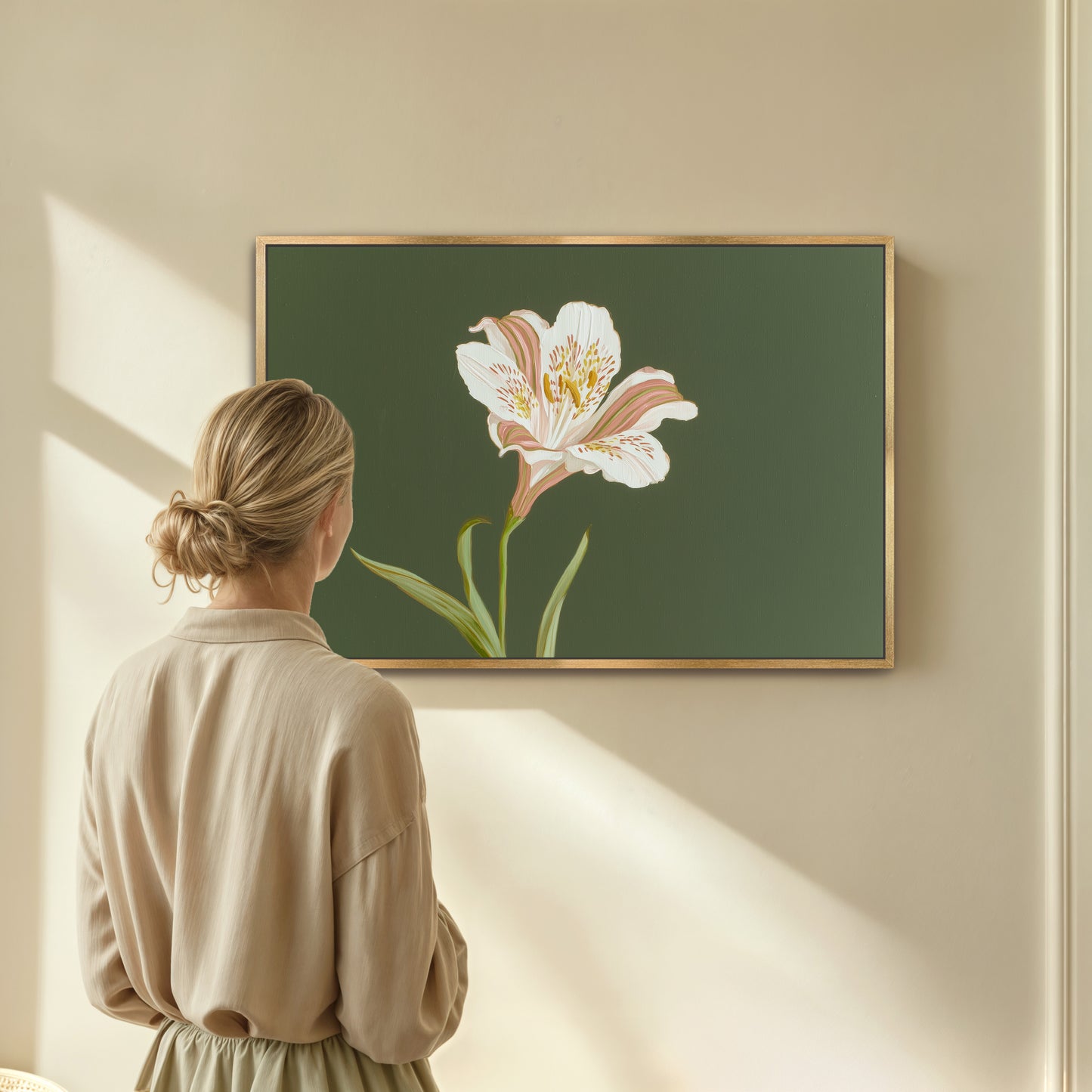 Woman looking at elegant white lily botanical painting on sage green background in gold frame