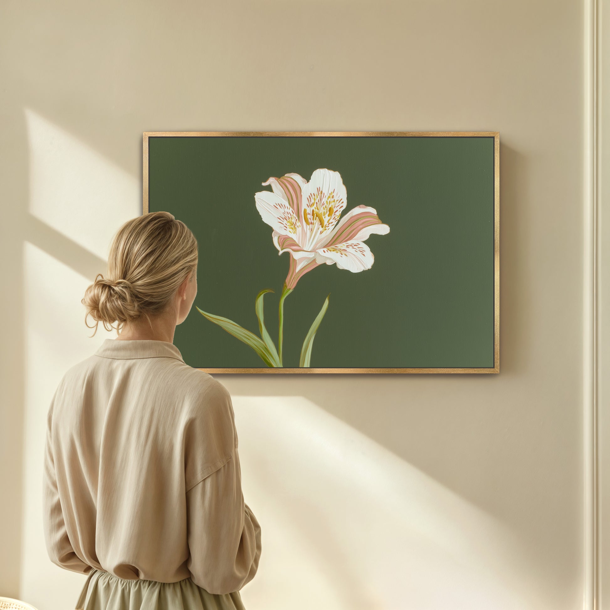 Woman looking at elegant white lily botanical painting on sage green background in gold frame